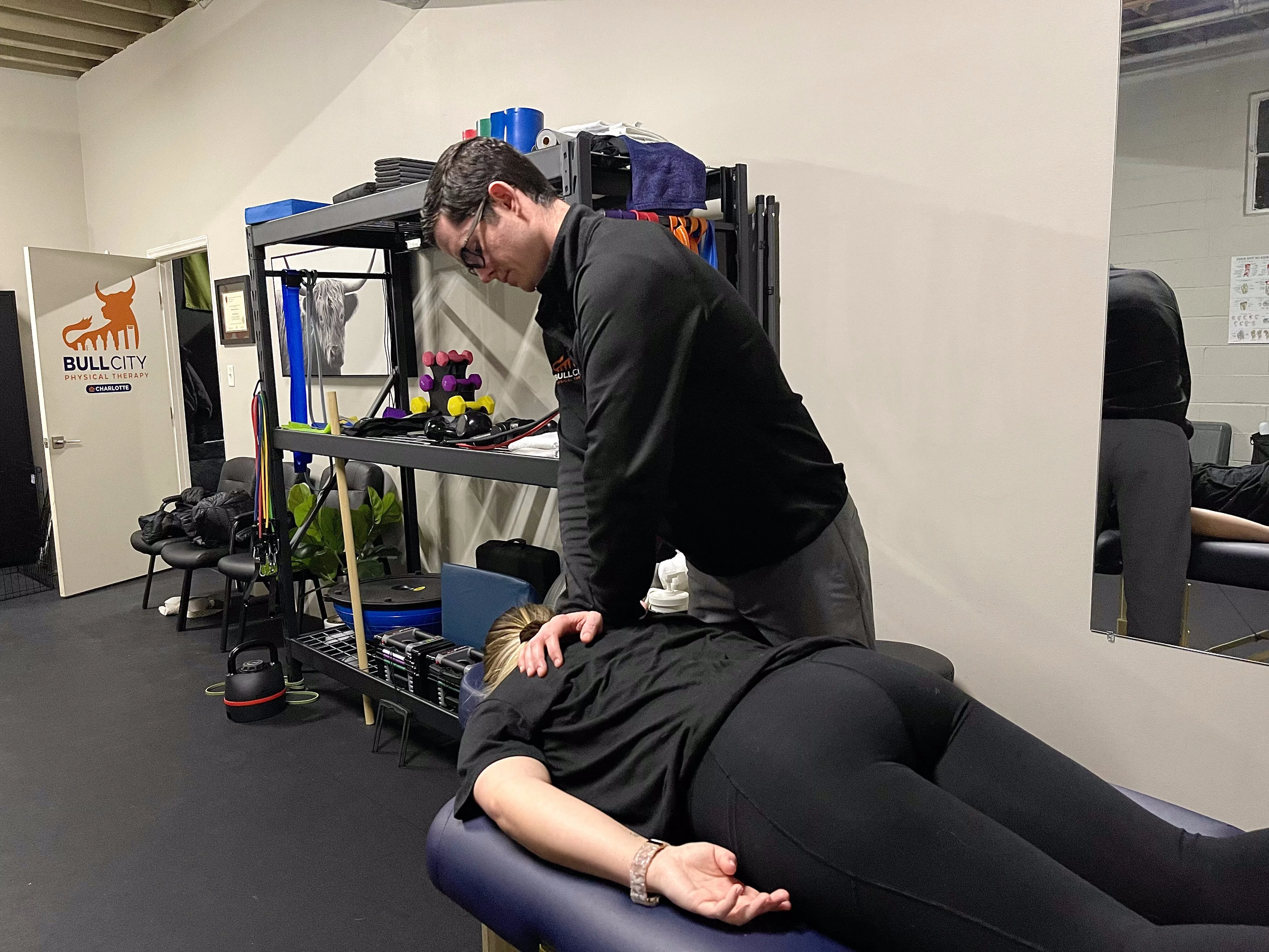 Physical therapist performing manual therapy on a female patient's back in a well-equipped clinic, highlighting advanced rehabilitation techniques.