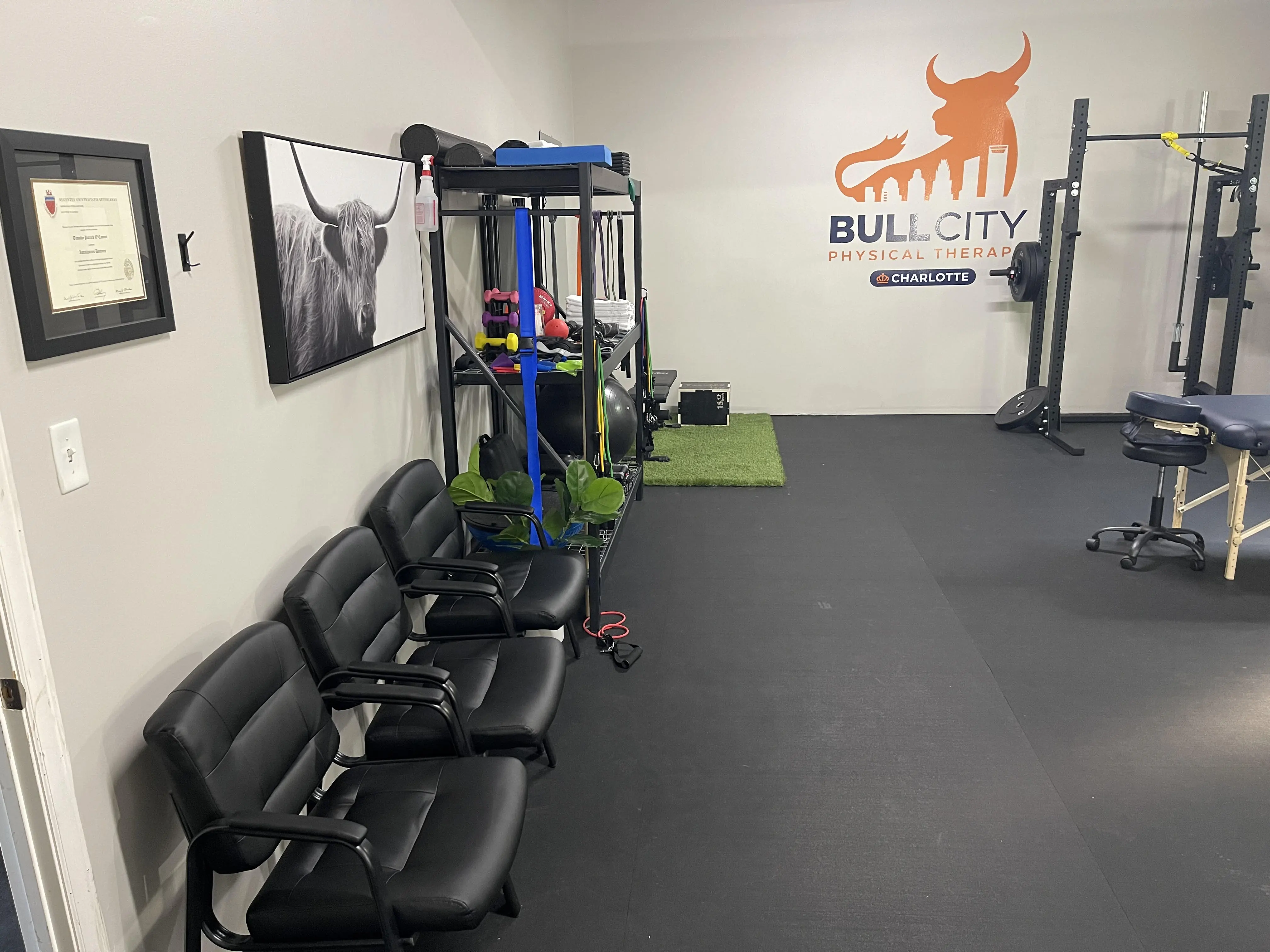 Modern physical therapy clinic interior featuring black waiting chairs, advanced gym equipment, and motivational wall art.